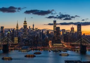 A scenic view of Gantry Plaza State Park in Long Island City showing industrial cranes and the NYC skyline at sunset.