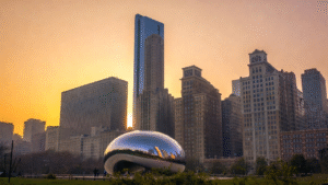The Cloud Gate sculpture in Millennium Park with the Chicago skyline and sunset in the background.